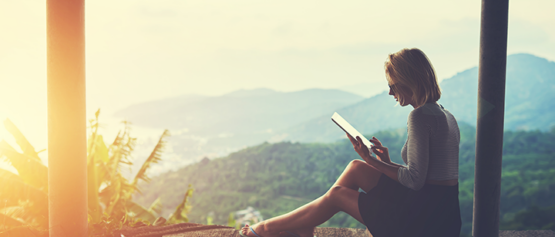 a woman using a tablet, while looking out her hotel window